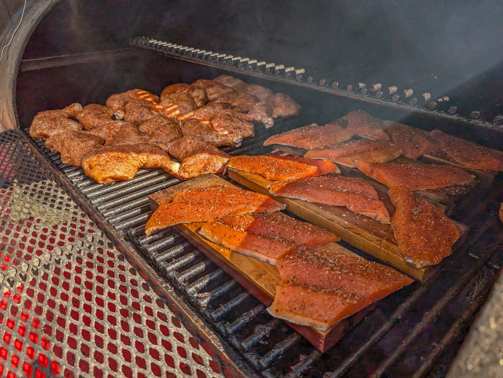 Chicken and salmon cooking on the grill with smoke rising